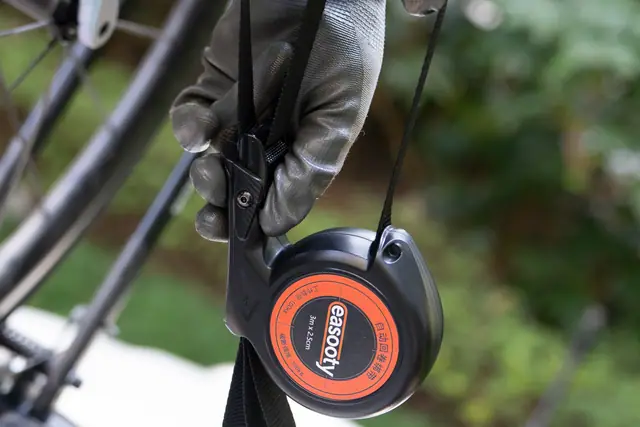 Mano tensando una cinta negra a través de un carrete de recogida automática junto a una bicicleta