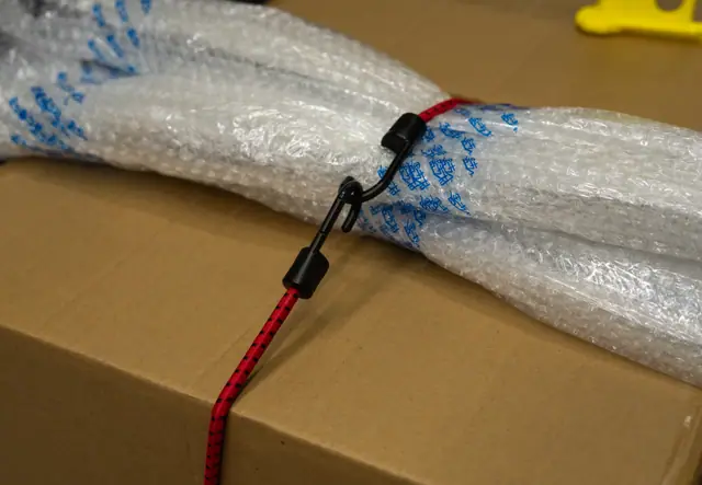 Red elastic strap holding a bubble-wrapped bundle against a carton
