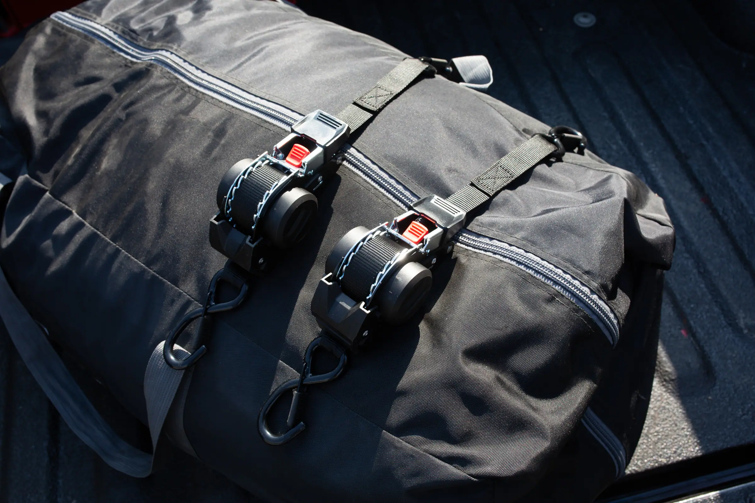 Deux sangles à cliquet à rappel automatique serrées sur un sac de voyage dans la benne d’un pick-up