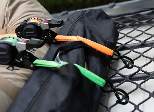 Two self-retracting ratchet straps fastening soft bags to a truck bed cargo net