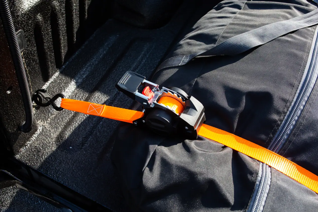Sangle à cliquet à rappel automatique accrochée au rail de benne d’un pick-up sur un sac souple