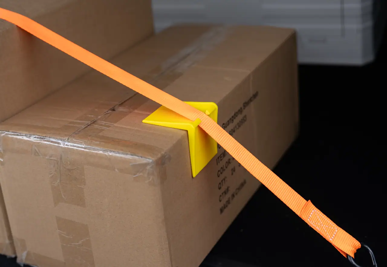Carton en entrepôt arrimé par une sangle passée dans une protection d’angle en ABS jaune